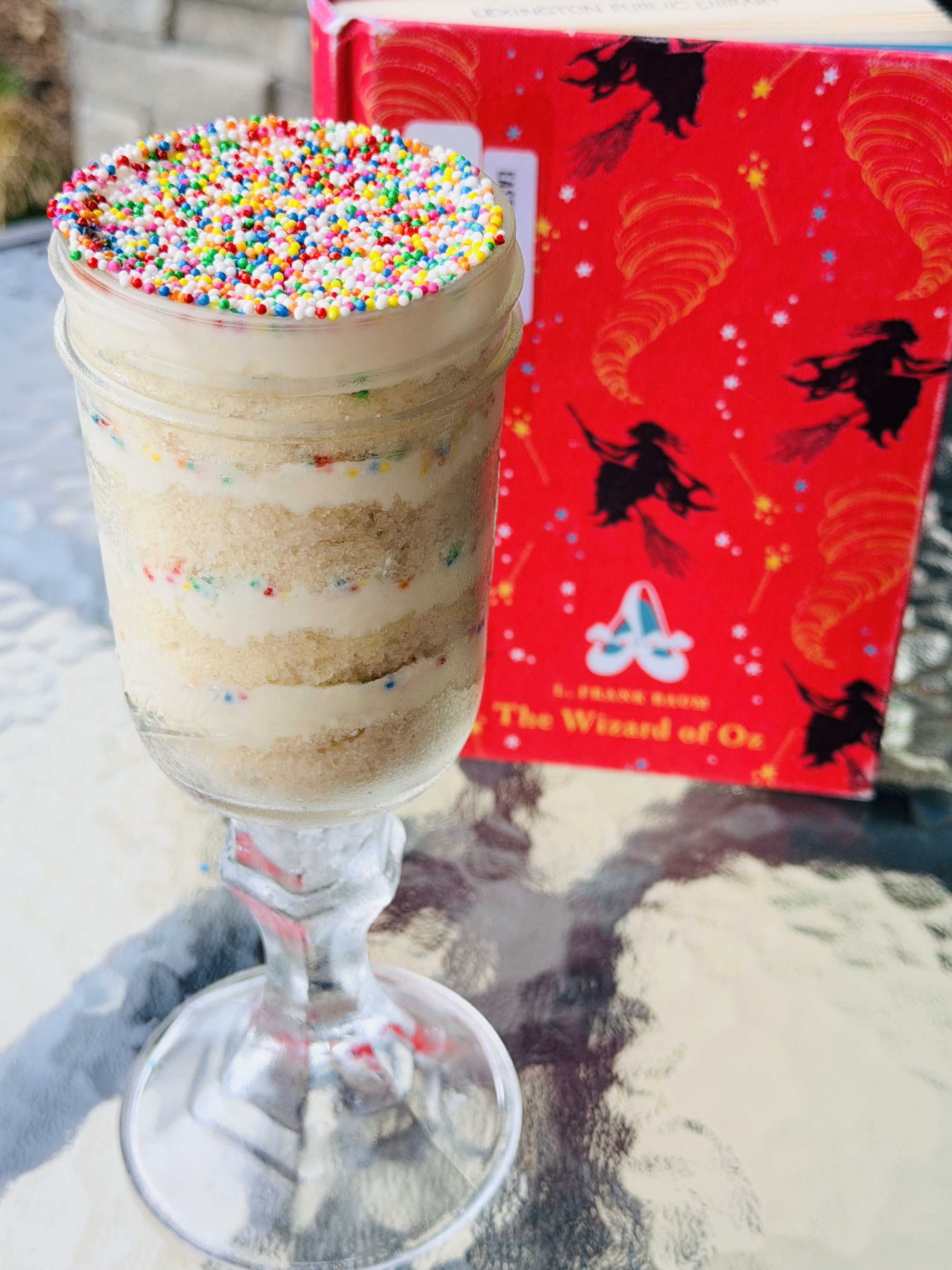 A sprinkle-topped funfetti cake layered in a jar beside a red vintage copy of The Wizard of Oz